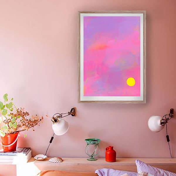 Pink and purple abstract art with yellow sunshine in an oak frame on a pale peach wall